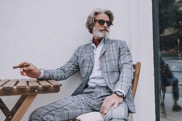 Elegant gentleman sitting with cigar outdoors stock photo