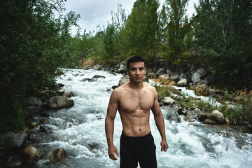 Kazakh muscular athlete man trains and exercises by the river in nature. Asian handsome does extreme fitness workout outdoors