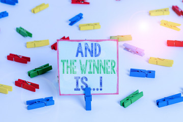 Word writing text And The Winner Is. Business photo showcasing announcing who got first place at competition or exam Colored clothespin papers empty reminder white floor background office