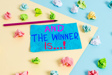Conceptual hand writing showing And The Winner Is. Concept meaning announcing who got first place at competition or exam Colored crumpled paper empty reminder blue yellow clothespin