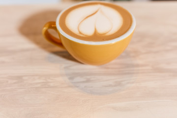 Magnificent yellow small size cup of aromatic fresh cappuccino or latte stands on wooden light coloured counter in modern coffee house, coffee art concept