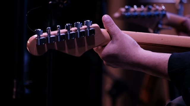 Guitar player. Close-up. The left male hand clamps the strings on the fretboard of a six-string guitar. Back view. Musical concert or party.