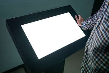 Man looking at white blank interactive touchscreen display of electronic multimedia kiosk in dark...
