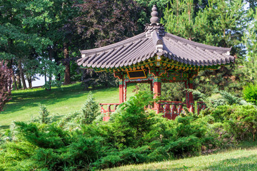 Fototapeta na wymiar Oriental-style gazebo with colorful decorations, lit by beams of light, among trees and bushes in the garden