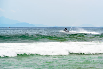 Black dressed man jumps on the jet ski above the sea waves