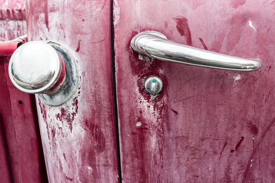 A door handle and fuel cap on the side of a red, antique pickup truck.
