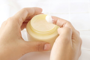 Side view of close up woman finger applying yellow cream in jar on white fabric background