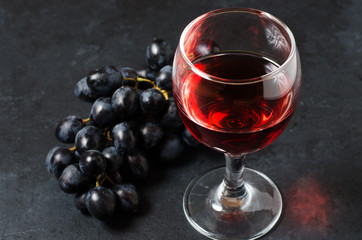 Red wine in a glass, a bunch of grapes. Dark background.