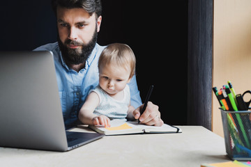Man and little baby sitting in front of laptop. Serious and busy father with small child on his...