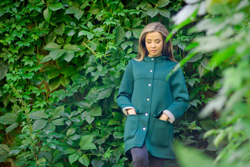 Portrait of a beautiful girl in a green coat on a background of ivy .