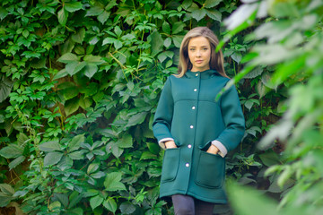 Portrait of a beautiful girl in a green coat on a background of ivy .