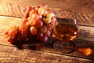 Cognac or Brandy in a glass and fresh grapes, still life in rustic style, vintage wooden background, selective focus.