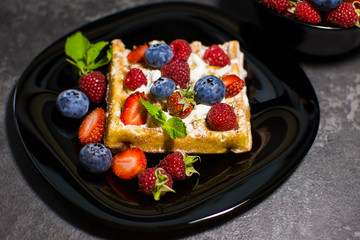 Belgian waffles with raspberries, strawberries and blueberries on a black plate. Selective focus.
