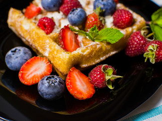 Belgian waffles with raspberries, strawberries and blueberries on a black plate. Selective focus.