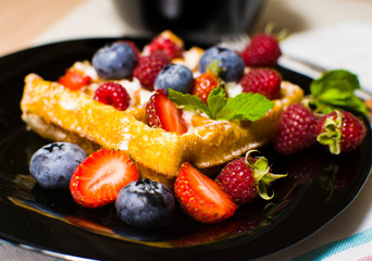 Belgian waffles with raspberries, strawberries and blueberries on a black plate. Selective focus.