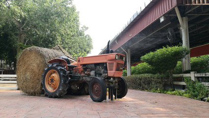 a orange old tractor with a big roll of straw.