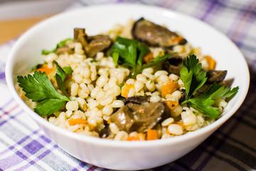 Vegetarian crumbly pearl barley porridge with mushrooms vegetables and herbs in a white plate
