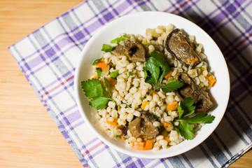Vegetarian crumbly pearl barley porridge with mushrooms vegetables and herbs in a white plate