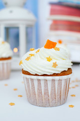 Cupcake with cream, orange candied fruit and gold confectionery sprinkling, lantern with light. Picture for a menu or a confectionery catalog.