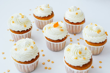 Group of cupcakses with cream, orange candied fruit and gold confectionery sprinkling at white table background. Picture for a menu or a confectionery catalog.