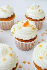 Group of cupcakses with cream, orange candied fruit and gold confectionery sprinkling at white table background. Picture for a menu or a confectionery catalog.
