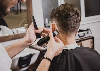 Fototapeten Junger Mann mit trendigem Haarschnitt im Friseurladen. Der Friseur macht die Frisur und den Bart. © romaset