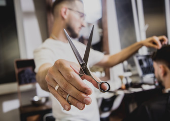 Young man with trendy haircut at barber shop. Barber does the hairstyle and beard trim.