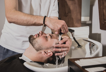 Young man with trendy haircut at barber shop. Barber washes customer head.