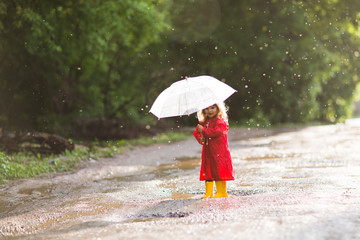 Happy child  with an umbrella playing also walks on pools in the autumn outdoors