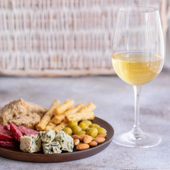 Glass of White wine and wood plate with antipasti. Blue cheese, olives, baguette slices, dry cured sausages and nuts. Wine snacks set background.