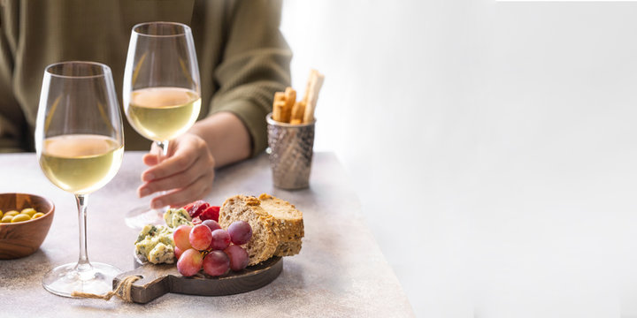 .Woman holding glass of white wine in the restaurant. Different snacks, Blue cheese, olives, baguette slices and cured meat. Tasting party lifestyle background for Banner with copy space.