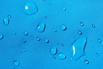 Closeup of water drops on bright blue fabric with waterproof design to protect fabric of the cloth from humidity and to offer easy cleaning to users Fabric texture with design and background concept
