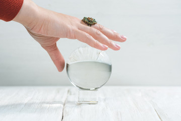 Crystal ball and fortune teller hand on white wooden table background.