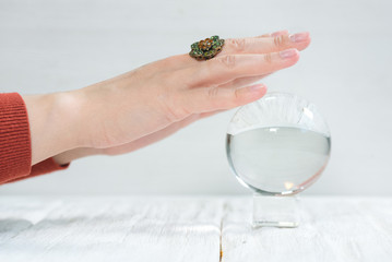 Crystal ball and fortune teller hand on white wooden table background.