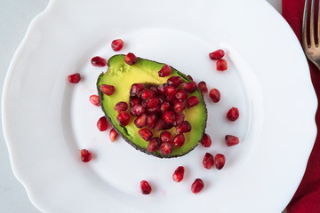 Red garnet seeds and half of avocado fruit on the white plate top view