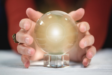 Crystal ball and fortune teller hand on white wooden table background.