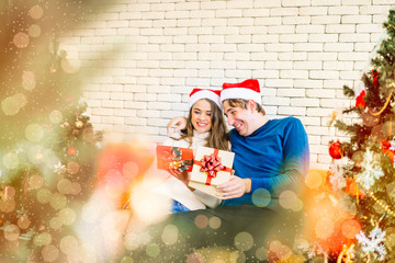 Young couple caucasian lovers sit on couch with presents in hands together in house decorated with Christmas trees. Exchanged gifts, smiling faces Happy and excited A festival of happiness with family