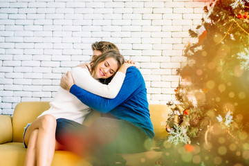 Young couple Caucasian lovers sitting on couch, love hug together to thanks for taking care in house decorate with Christmas trees. Celebration festival with family, Santa gifts, food celebrating 