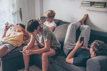 Group of teenager using smartphone sitting on a sofa at home. Young boys and a girl sharing photo...