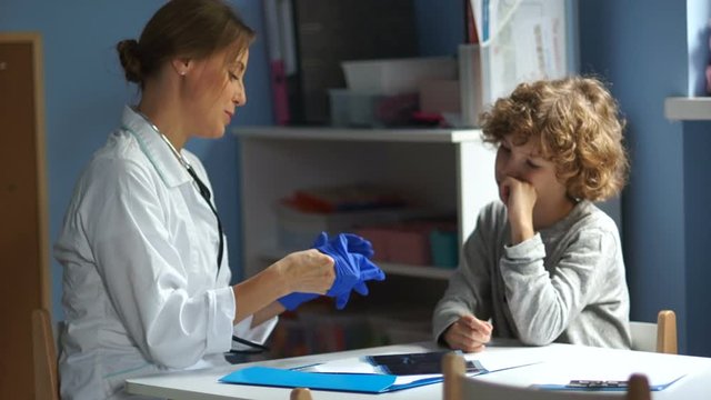 Curly boy teenager at a reception at the pediatrician. Female doctor listens to the lungs and bronchi in a teenager