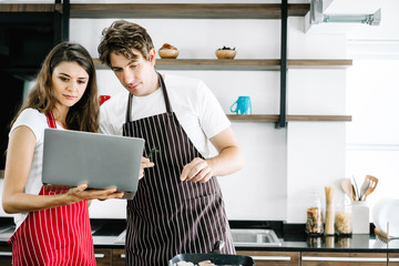 Cooking online training, young couple using computer notebook to follow step to cook. Looking at screen to listen chef advisory. Family relationship activity while resting at home, eating together.