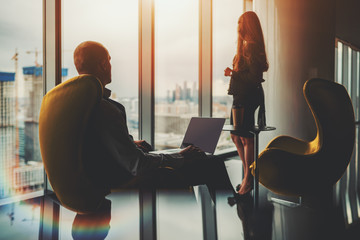 Two silhouettes of business partners on the top floor of a luxurious office skyscraper in front of...