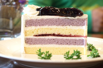 Close up blueberry sponge layer cake topping by blueberry sauce on white plate on wooden table in restaurant, look soft and delicious