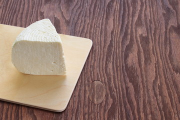Adyghe cheese on a cutting Board. brown wood background