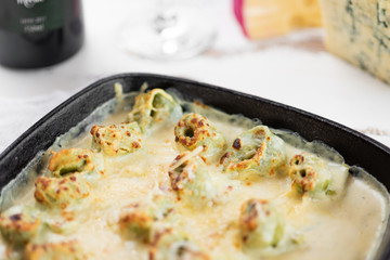 Homemade capeletti pasta with bechamel sauce in an black iron pan. Italian cuisine