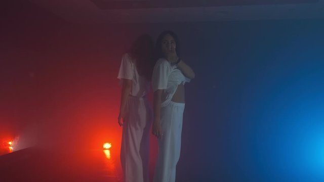 Young girls in white dancing hip hop in smoky studio with blue and red lights background. Woman performs modern dance indoors in slow motion. 4k, UHD