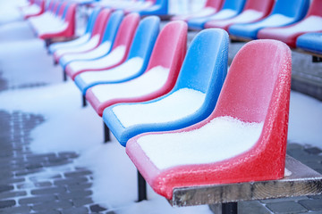Snow-covered multi-colored seats in the stadium in winter. Snowfall interferes with sports....