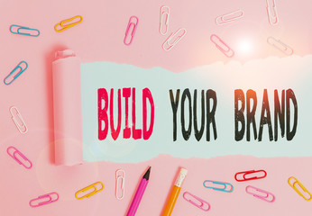 Handwriting text writing Build Your Brand. Conceptual photo enhancing brand equity using advertising campaigns Stationary and torn cardboard placed above a plain pastel table backdrop