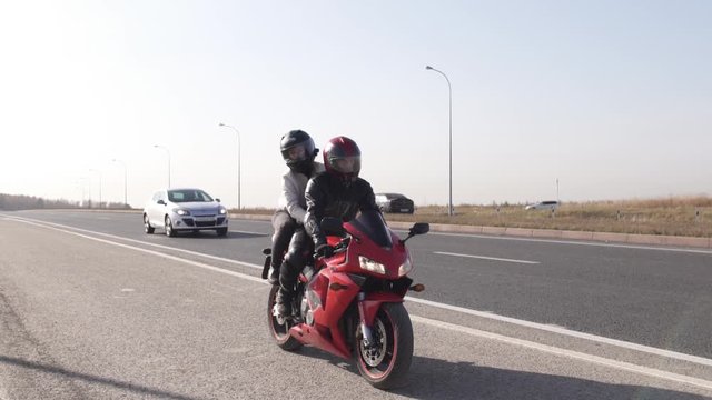 A man and a young woman in sports equipment and a helmet ride on the road on a red sports motorcycle