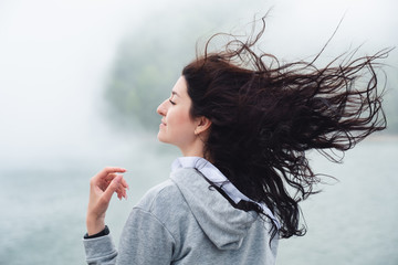 Young caucasian woman posing in fog, her hair fluttering in the wind.Close up portrait of beautiful millennial girl in windy summer day.